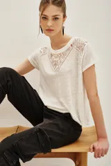 Remera de lino color blanco con detalle de encaje en el escote y hombros, de corte holgado y mangas cortas.