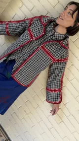 Chaqueta de paño reversible con diseño de cuadros en el interior. Presenta bordes con costuras decorativas en hilo rojo y mangas con puños vueltos que dejan ver el estampado interior.