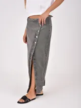 Falda larga de denim color gris oscuro, con diseño cruzado frontal (wrap) que se ajusta con botones plateados, creando una abertura pronunciada.