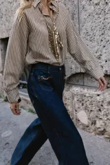 Jeans de mezclilla azul oscuro, tiro medio, corte pierna ancha (wide leg). Presenta bolsillos delanteros de parche con detalle de cadena metálica decorativa.