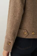 Campera de lana fina sin teñir, con cuello alto, cierre frontal completo y diseño de corte recto con pespuntes decorativos en puños, ruedo y cuello.