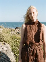 Blusa sin mangas color marrón, confeccionada en lino, con cuello alto plisado, diseño asimétrico con botones forrados al tono y volados laterales.