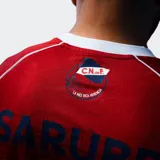 Camiseta de fútbol Umbro del Club Nacional de Football, modelo Away 2026. Diseño en color rojo con detalles en azul y blanco en el cuello y mangas. Incluye logo de Umbro, escudo del club y sponsor Antel en el frente.