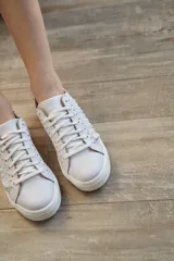 Zapatillas blancas de cuero con base ultraliviana y plataforma de 3cm. Detalle de talonera dorada y tachas metálicas plateadas.