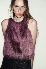 Top de cuello redondo y manga sisa, confeccionado con un acabado de flecos largos en color lila. Presenta un diseño recto con cierre en la espalda mediante abertura y botón oculto.