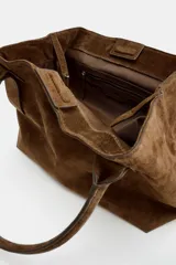Bolso tipo shopper de piel en color marrón, con doble asa de hombro, bolsillo interior con cremallera y doble sistema de cierre con botón imantado y tira con botón metálico.