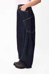 Jean de corte amplio y tiro medio, confeccionado en denim azul oscuro con costuras a contratono en color blanco. Presenta un diseño de pierna curva con bolsillos laterales integrados.