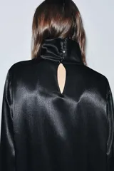 Blusa de Zara Woman Collection confeccionada en viscosa, con cuello alto, manga larga y diseño asimétrico en el bajo. Presenta un acabado satinado y cierre en la espalda.