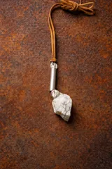 Collar con tiento de cuero marrón y dije con forma irregular, compuesto por un cilindro de metal dorado, una piedra amatista y una piedra de cuarzo transparente.