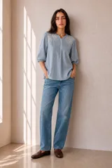 Blusa a rayas verticales en tonos rosados y blancos, con cuello redondo y cierre frontal parcial con botones. Presenta delicados detalles bordados en los hombros y mangas tres cuartos abullonadas con puños elásticos.