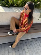 Sweater de punto con cuello alto, diseño geométrico con rayas diagonales en tonos naranja, marrón y blanco.
