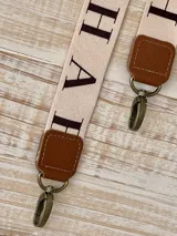 Correa de repuesto para cartera, de tela color beige con rayas blancas y negras. Incluye herrajes metálicos color bronce y apliques de cuero sintético color marrón.