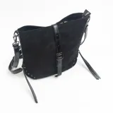 Cartera de hombro color negro, confeccionada en material tipo gamuza, con correa ajustable y detalles de tachas metálicas en las esquinas inferiores. Presenta una tira vertical central con hebilla decorativa y tiras laterales colgantes.