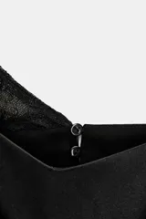 Vestido midi negro de satén con escote asimétrico y tirantes finos. Presenta detalle de encaje en el escote y en el ruedo. Cuenta con abertura en la espalda y cierre con cremallera oculta y botones.