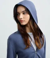 Campera corta con capucha fija, cierre frontal con cremallera y mangas largas, confeccionada en tejido modal con acabado satinado.