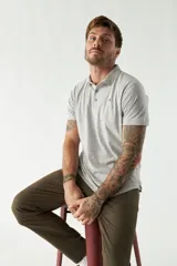 Pantalón chino color verde militar, de corte slim, con bolsillos laterales y traseros. Se ajusta a la cintura con cinturón de cuero marrón.