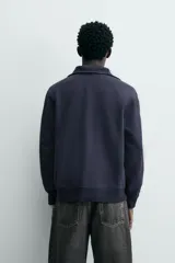 Sudadera de calce relajado color azul marino, con cuello alto y cierre frontal mediante alamares metálicos. Presenta manga larga y terminaciones en rib en puños y cintura.