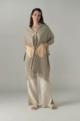 Chal de lana fina sin teñir con diseño de cuadros sutiles, cierre frontal con alamar y bolsillos de cuero metalizado. Presenta terminaciones con flecos en el ruedo y un calce estructurado en los hombros.