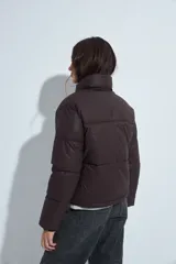 Campera puffer de nylon color marrón oscuro, con cuello alto, cierre frontal y puños elásticos. Diseño acolchado de volumen ligero.