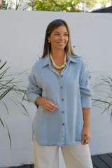 Camisa de jean en tono celeste claro, de corte holgado y diseño oversize. Presenta cuello clásico, cierre frontal con botones y mangas largas con puños con detalle de volado sutil.