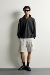 Bermuda cargo color negro de corte relaxed fit, confeccionada en tejido de algodón con elasticidad y efecto lavado. Cuenta con cintura elástica ajustable con cordón, bolsillos frontales y bolsillos laterales tipo cargo con solapa en las perneras.