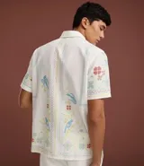 Camisa blanca de lino y algodón, de corte comfort, cuello inglés y abotonado frontal. Presenta manga corta y un bordado floral multicolor con motivos de aves y flores.