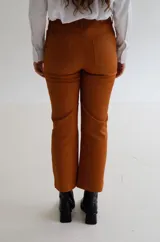 Pantalón cropped de tiro medio con acabado engomado, corte recto y bolsillos laterales. Presenta cierre frontal con botón y costuras a tono.