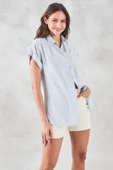 Blusa de viscosa rayada en blanco y celeste, con cuello camisero, mangas cortas con dobladillo y botones frontales.