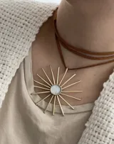 Collar tipo gargantilla con dije de bronce en forma de sol con centro de nácar, montado sobre un tiento de cuero sintético color marrón camel.