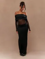 Vestido largo negro con escote bardot, mangas largas de tul semitransparente y silueta ajustada.