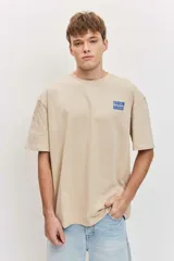 Remera de corte oversize color blanco tiza, de manga corta y cuello redondo, con pequeño estampado gráfico azul en el pecho.