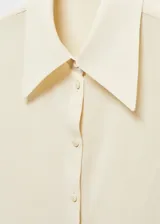 Camisa color crema de corte recto, cuello camisero y mangas largas con puños abotonados.
