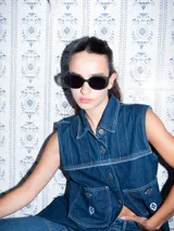 Vestido corto de jean color gris oscuro con efecto acid wash, sin mangas, con cuello camisero y cierre frontal de botones. Incluye dos bolsillos en el pecho con solapa y pespuntes decorativos.