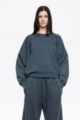 Buzo de corte globo confeccionado en algodón, con escote caja y mangas largas ranglán. Presenta un diseño de calce relajado con volumen y un pequeño logo bordado en el pecho.