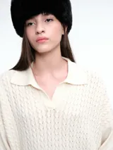 Sweater de tejido de punto color beige, con diseño de trenzas en el frente y mangas lisas. Presenta cuello polo con escote en V y puños y ruedo acanalados.