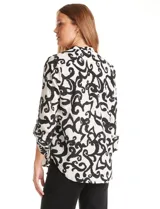 Blusa de gasa estampada en blanco y negro con diseño abstracto. Cuello a la base, escote en V y mangas largas regulables con presilla y botón.