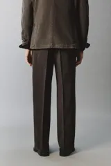 Pantalón relaxed fit de traje color marrón oscuro, confeccionado en tejido con mezcla de algodón. Cuenta con bolsillos frontales, bolsillos traseros de doble vivo con botón y efecto lavado. Cierre frontal con cremallera y botón.