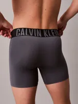 Pack de tres boxers largos Calvin Klein de microfibra, con talle medio y cinturilla elástica distintiva con el logo de la marca. Incluye un bóxer negro con elástico negro y letras blancas, un bóxer gris con elástico negro y letras grises, y un bóxer azul con elástico negro y letras azules.