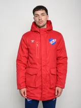 Parka larga de abrigo color rojo con capucha, cierre frontal con solapa, bolsillos frontales con solapa y bolsillo superior con cierre. Presenta el escudo del Club Nacional de Football y el logo de Umbro bordados en el pecho.
