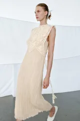 Vestido midi de viscosa con efecto arrugado, cuello redondo y diseño sin mangas. Presenta una sobrecapa superior con bordados detallados y entredoses, con cordones laterales ajustables terminados en borlas.