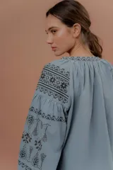 Blusa celeste de estilo bohemio con mangas amplias abullonadas y delicados bordados en contraste en los hombros y mangas.