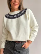 Sweater de punto color blanco con cuello redondo y detalle de guarda decorativa estilo nórdico en tonos oscuros alrededor del escote. Presenta mangas largas con puños acanalados y un corte holgado.