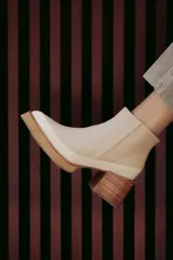 Botín de cuero color beige con puntera charolada, cierre lateral con cremallera y tacón ancho de madera.