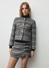 Chaqueta de tweed con cuello redondo, cierre frontal de botones metálicos y cuatro bolsillos de solapa en la parte delantera. Presenta un diseño recto de manga larga con acabado desflecado en el bajo.