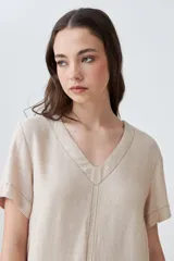 Vestido corto color beige melange, de lino, con cuello en V y mangas cortas. Presenta pespuntes verticales en contraste.