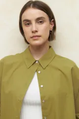 Camisa de corte clásico y holgado, confeccionada en tela blanca, con cuello camisero, cierre frontal de botones de nácar y mangas largas con puños abotonados.