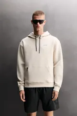 Sudadera de hombre Zara Athleticz de ajuste relajado (relaxed fit), color marrón, confeccionada en tejido técnico compacto con mezcla de algodón y elasticidad. Cuenta con cuello con capucha ajustable con cordones negros, manga larga, bolsillo frontal tipo canguro con un pequeño bolsillo termofijado con cierre, y acabados con rib en puños y cintura.
