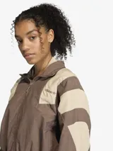 Campera deportiva Adidas de corte oversize, con cierre frontal completo y cuello alto. Presenta un diseño de bloques de color en tonos marrón y beige, inspirado en el estilo Equipment de los años 90, con puños y cintura elásticos.