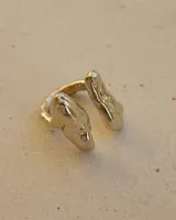 Anillo de diseño orgánico y macizo con forma irregular, elaborado en metal con acabado brillante. Presenta una estructura abierta que permite su ajuste.