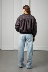 Campera bomber de gamuza con estampado animal print en tonos marrones. Presenta cierre frontal dorado, puños y cintura de tejido elástico negro, y bandas laterales negras en las mangas.